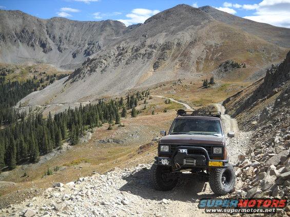 Brown Ford Bronco II with winch and roof rack on rocky mountain road