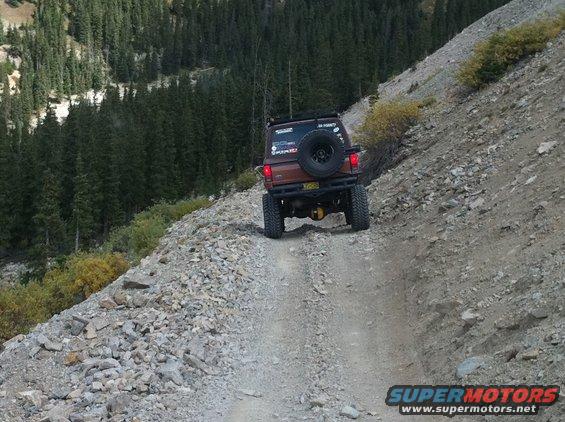 Brown Ford Bronco II driving on a rocky mountain road, rear view