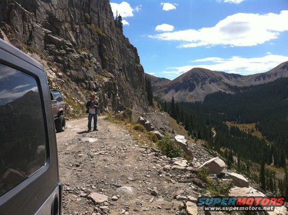 Dark SUV on a rocky mountain road with a person standing nearby