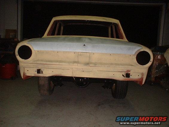 Car body in primer, front view, missing headlights and grille, undergoing restoration