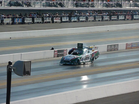 Funny car drag racer with green and white livery on track, spectators in background