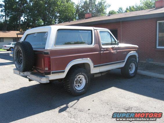 Brown and white Ford Bronco parked outside a brick building. Spare tire mounted on the rear