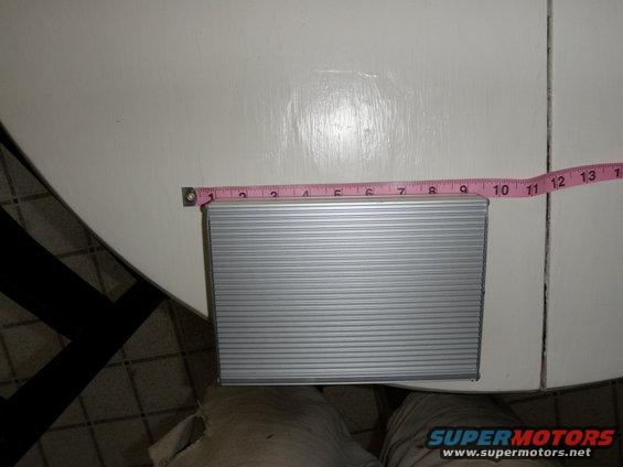 Silver rectangular object with horizontal ridges, being measured with a pink tape measure
