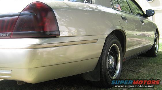 Tan 2000 Mercury Grand Marquis rear quarter panel and taillight, with a black mud flap and chrome hubcap