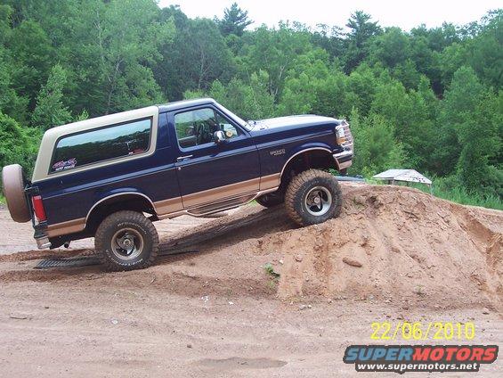 Blue and tan 1990 Ford Bronco climbing a dirt hill, side view