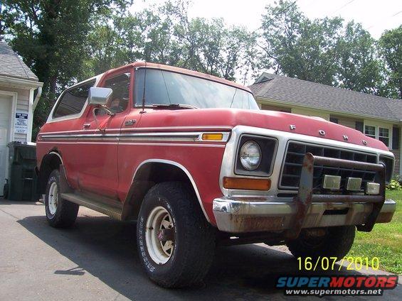 Red Ford Bronco with a brush guard and aftermarket lights. White wheels and chrome trim are visible