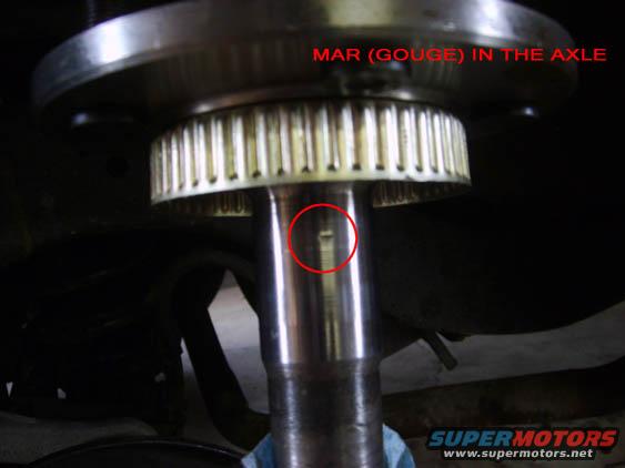 Close-up of a vehicle axle showing a mar or gouge, with text indicating 'MAR (GOUGE) IN THE AXLE'
