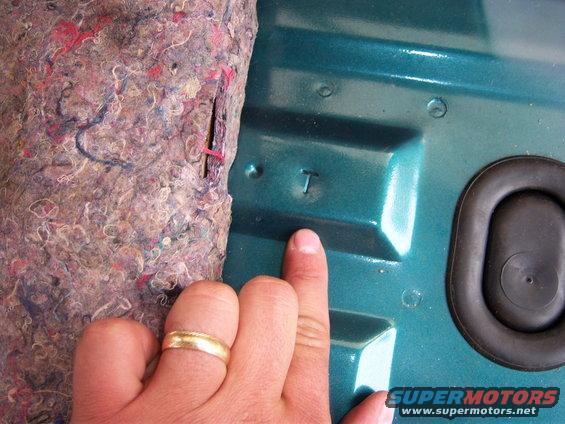 Teal interior panel with a finger pointing to a stamped letter T and a rubber grommet
