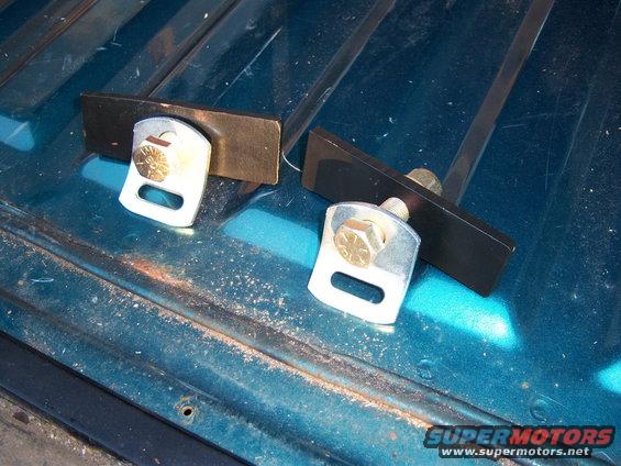 Two metal child seat tether anchors bolted to a teal surface with visible rust and wear