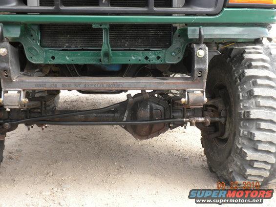 Front axle, suspension, and part of the grille of a modified off-road vehicle. Text on metal bar reads 'EURO USA 4500 B/T 4XPX1/6 FA03985'