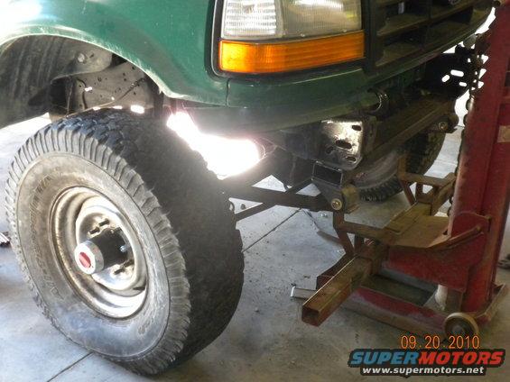 Green Ford F-Series truck front end with large tire and jack stand