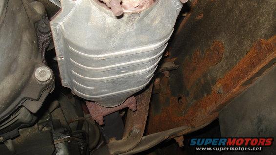 Close-up of a vehicle's exhaust system, showing a catalytic converter and rusted frame components