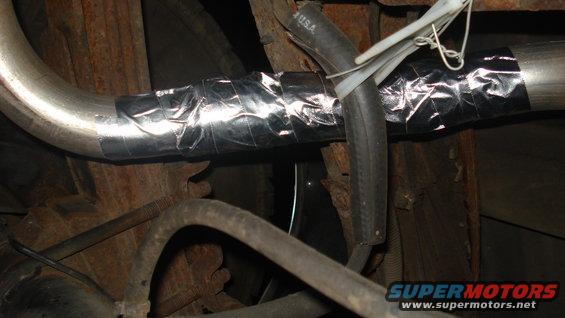 Exhaust pipe wrapped in silver tape with a black hose secured by zip ties