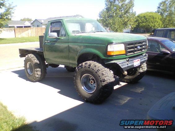 Green flatbed truck with large off-road tires, lifted suspension, and a custom bumper