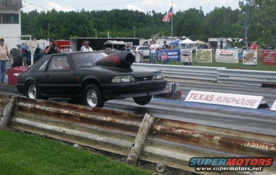 Black 1990 Ford Mustang drag car with a large hood scoop, on a drag strip