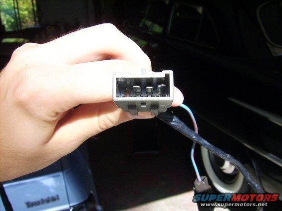 Hand holding a gray electrical connector with four pins and attached wires