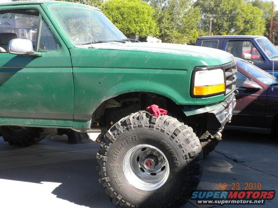 Green 1989 Ford Bronco front quarter view, lifted with large off-road tires. Another vehicle is parked behind it