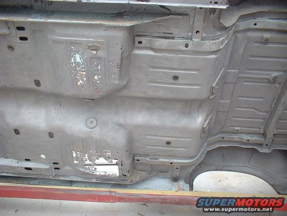 Underside of a car chassis, gray, showing rust and damage, viewed from below