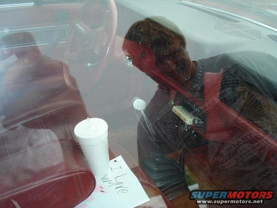 Interior shot of a car with a red steering wheel, a cup, and a note that says 'I Love Mom'