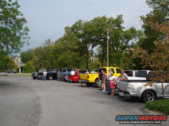 Several pickup trucks parked in a lot with people standing around them. The trucks appear to be from the late 1990s