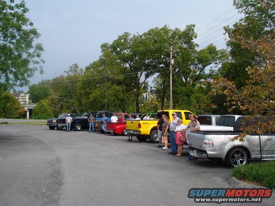 Several pickup trucks parked in a lot with people standing around them
