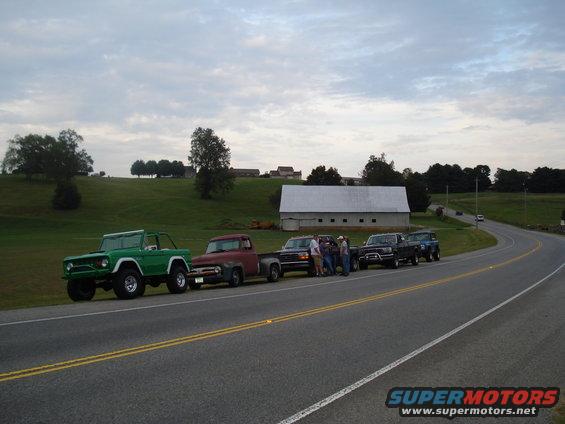 Green Ford Bronco and red Ford F-100 pickup truck parked side-by-side on a road