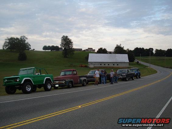 Green Ford Bronco, red Ford F-100, black Ford F-150, and blue Ford Bronco parked on roadside with people