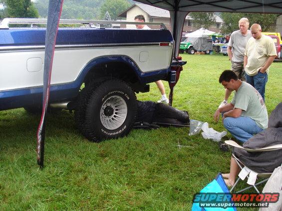 Side view of a blue and white Ford F-Series truck with a person working underneath