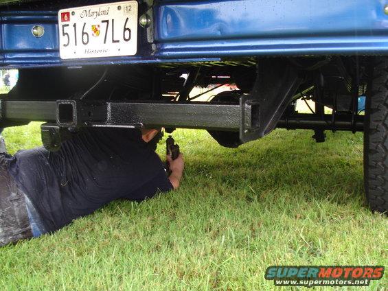 Man works on the hitch of a blue truck. Maryland license plate 516 7L6 is visible