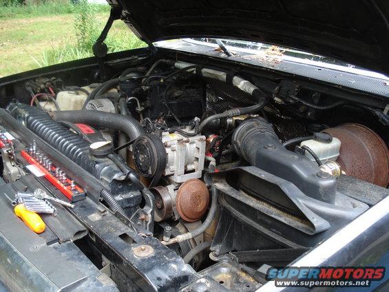 Engine bay of a truck with tools on the radiator. Air intake, AC compressor, and belts visible