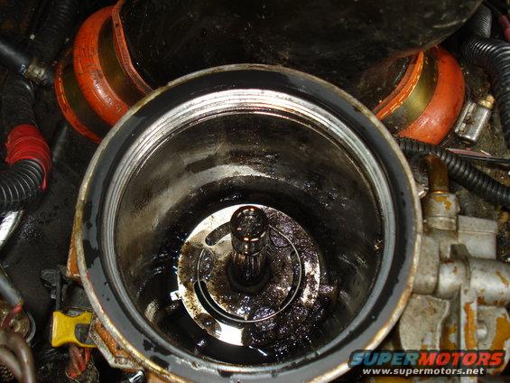 Open engine oil filter housing with dirty oil inside. Orange hose and black wiring visible