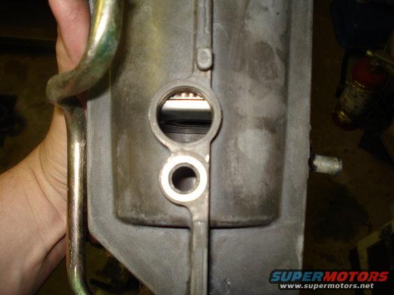 Gray metal engine component with two circular openings, one above the other. A hand holds a metal pipe