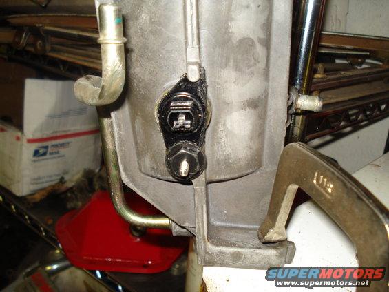 Close-up of a transmission housing with a sensor and a bolt. A clamp is attached to the housing