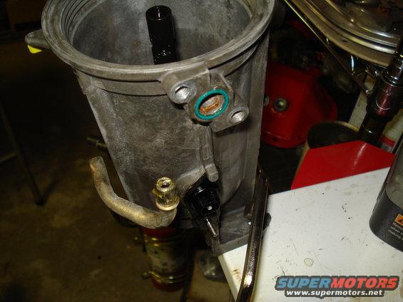 Close-up of an engine oil filter housing with a black sensor attached. A metal tube connects to the side