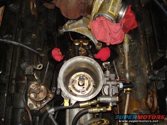 Engine fuel filter housing with red rags stuffed in openings. Supermotors.net logo visible