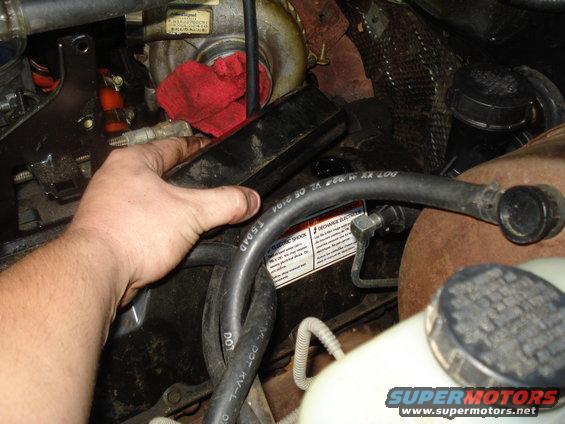 Hand reaching into engine bay near turbocharger and hoses