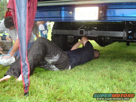 Man lying on grass working on the undercarriage of a blue truck