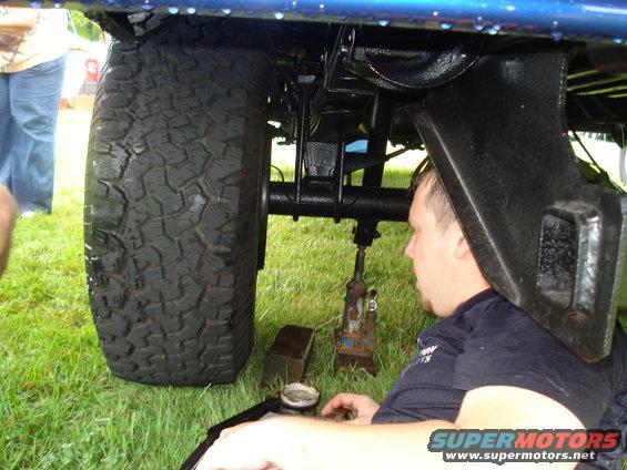 Undercarriage of a blue truck, showing a large tire and suspension components, with a man working below