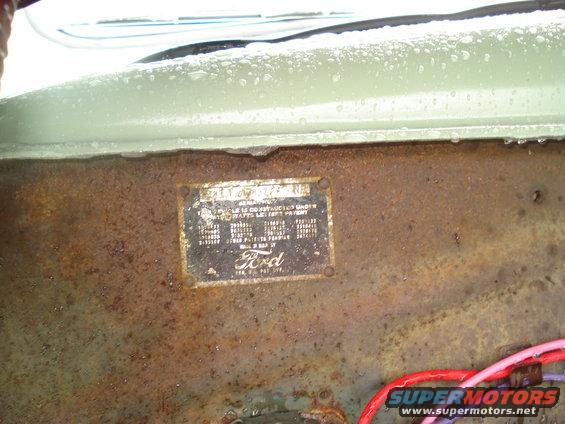 Close-up of a Ford VIN plate attached to a rusty metal surface, with some wires visible