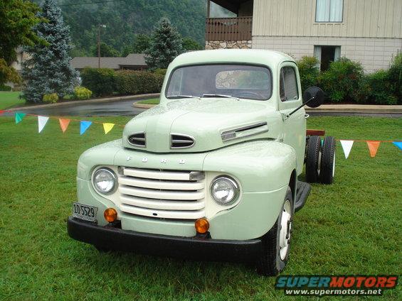 Light green 1950s Ford F-series truck with dual rear wheels parked on grass