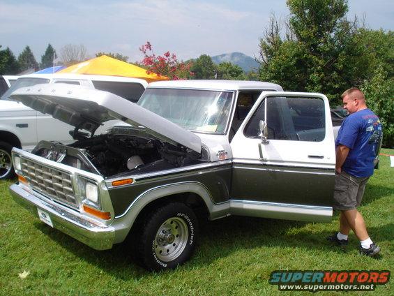 Two-tone 1970s Ford F-Series truck with hood open and driver's door ajar. Another white truck is partially visible behind it