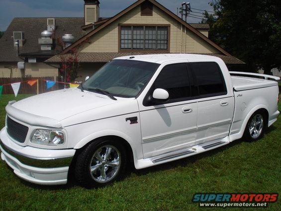 White pickup truck with custom body kit and chrome wheels parked on grass