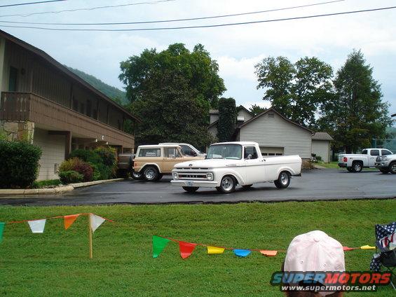 White 1960s pickup truck and tan SUV parked in front of a building