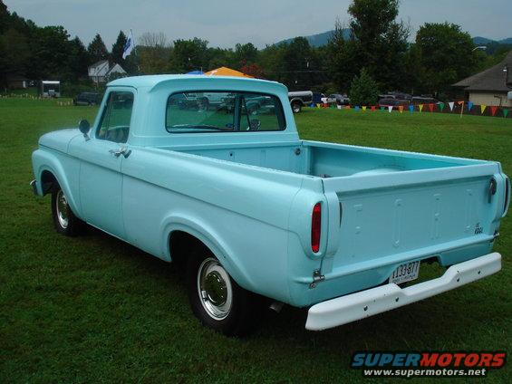 Light blue 1956 Ford F-100 pickup truck parked on grass, rear three-quarter view