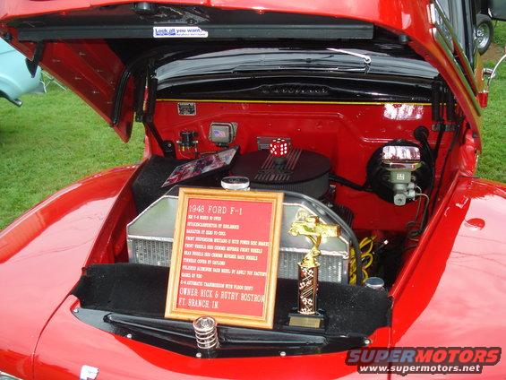 Red 1948 Ford F-1 engine bay with a framed document and trophy