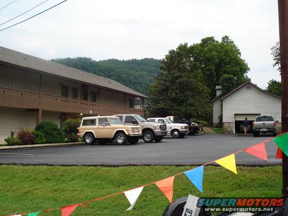 Tan Ford Bronco and several pickup trucks parked in a lot next to a building