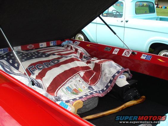 Red pickup truck bed with an American flag blanket and a light blue 1956 Ford F-100 in the background