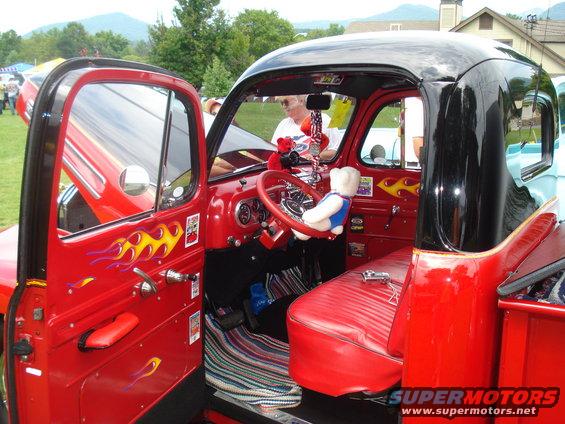 Red pickup truck interior with flames on doors and dashboard, teddy bear on steering wheel