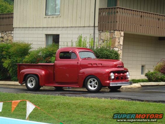 Red classic pickup truck with chrome wheels parked on asphalt in front of a building