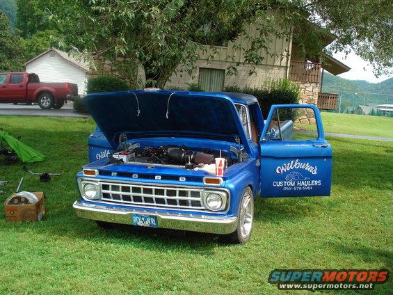 Blue Ford pickup truck with hood and driver's door open, showing engine and custom lettering